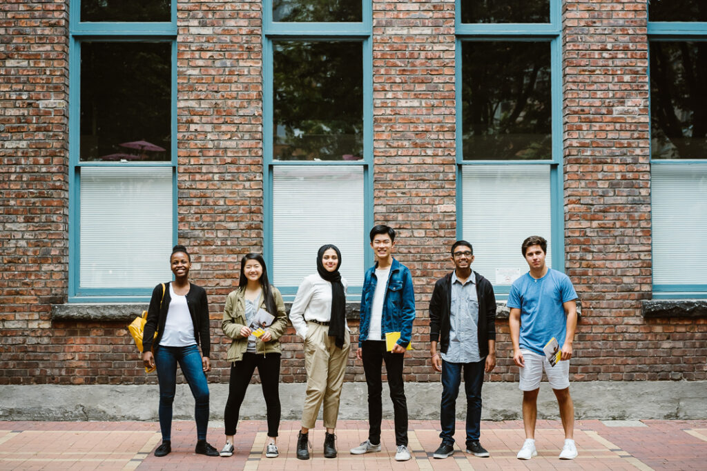 Six university students stand side-by-side agains a brick wall.