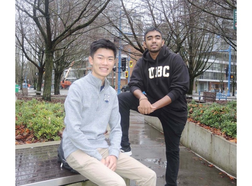 Two male students lounge outdoors in a Vancouver Park, facing the camera and smiling.