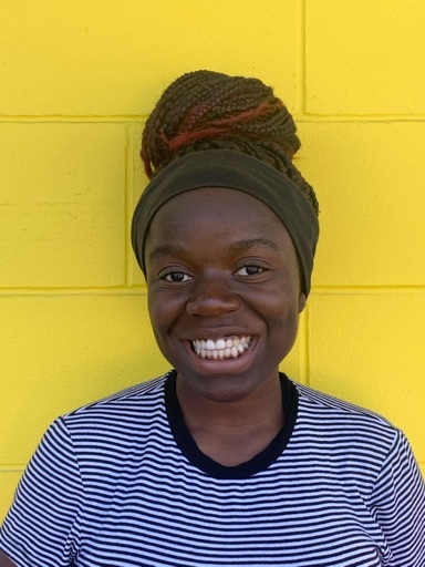Woman standing in front of yellow brick wall, smiling.