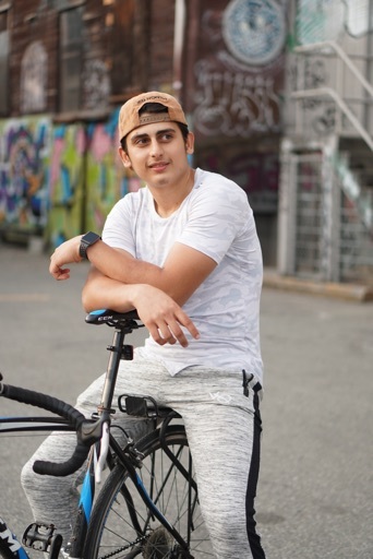 Young man with a backwards hat and white t-shirt seated, lounging on a bicycle.