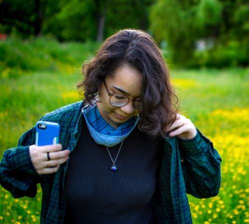 Student standing in a green field fixes their sweater, looking downwards.