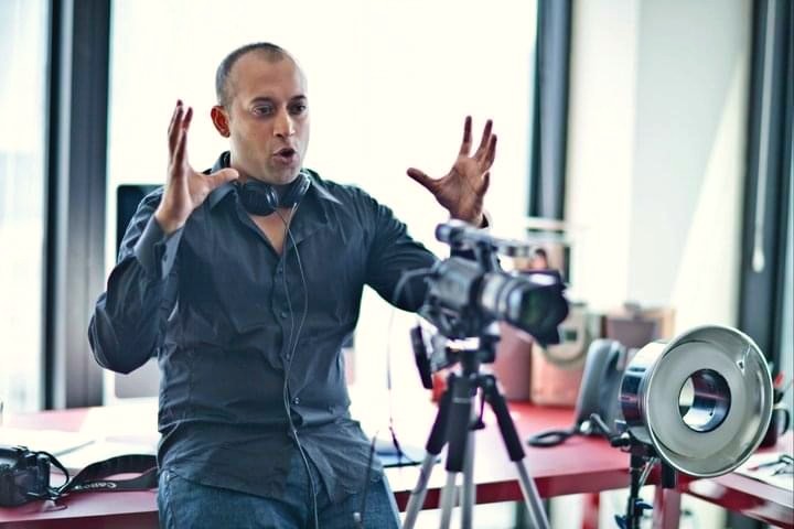 Man speaks expressively while operating video cameras.