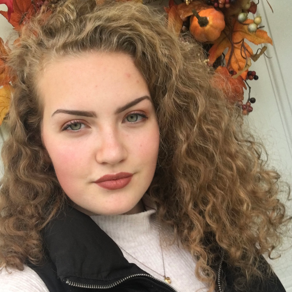 Selfie of a woman with curly hair wearing a black scarf.