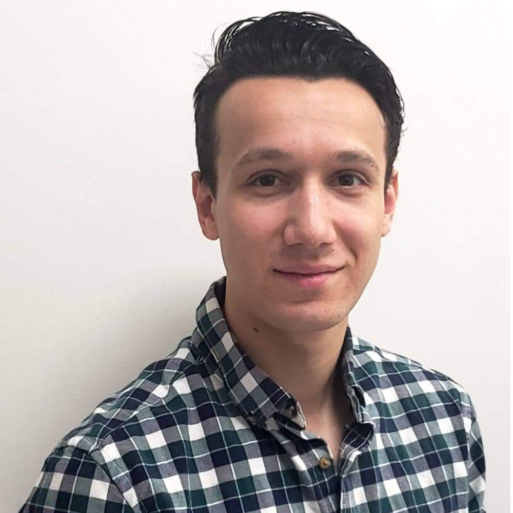 Young man in a dark plaid shirt smiles at the camera.