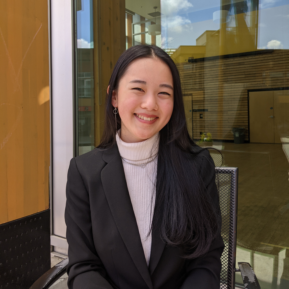 Young woman smiles at camera wearing a turtle neck and black blazer.