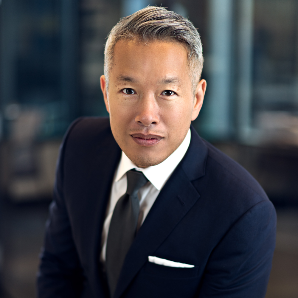Todd Yuen headshot in black suit with white pocket square.