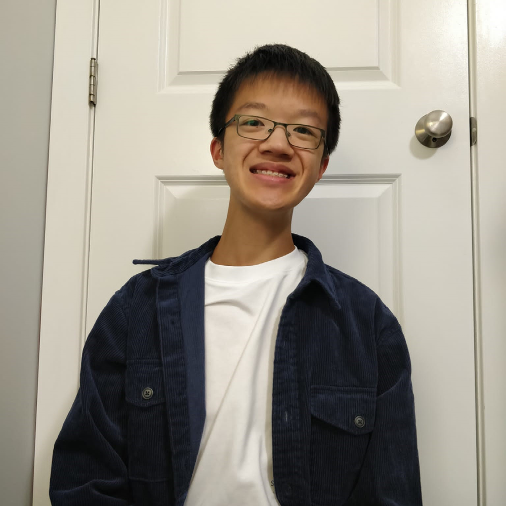Young Asian man wearing white t-shirt and dark jacket sits in front of white door.