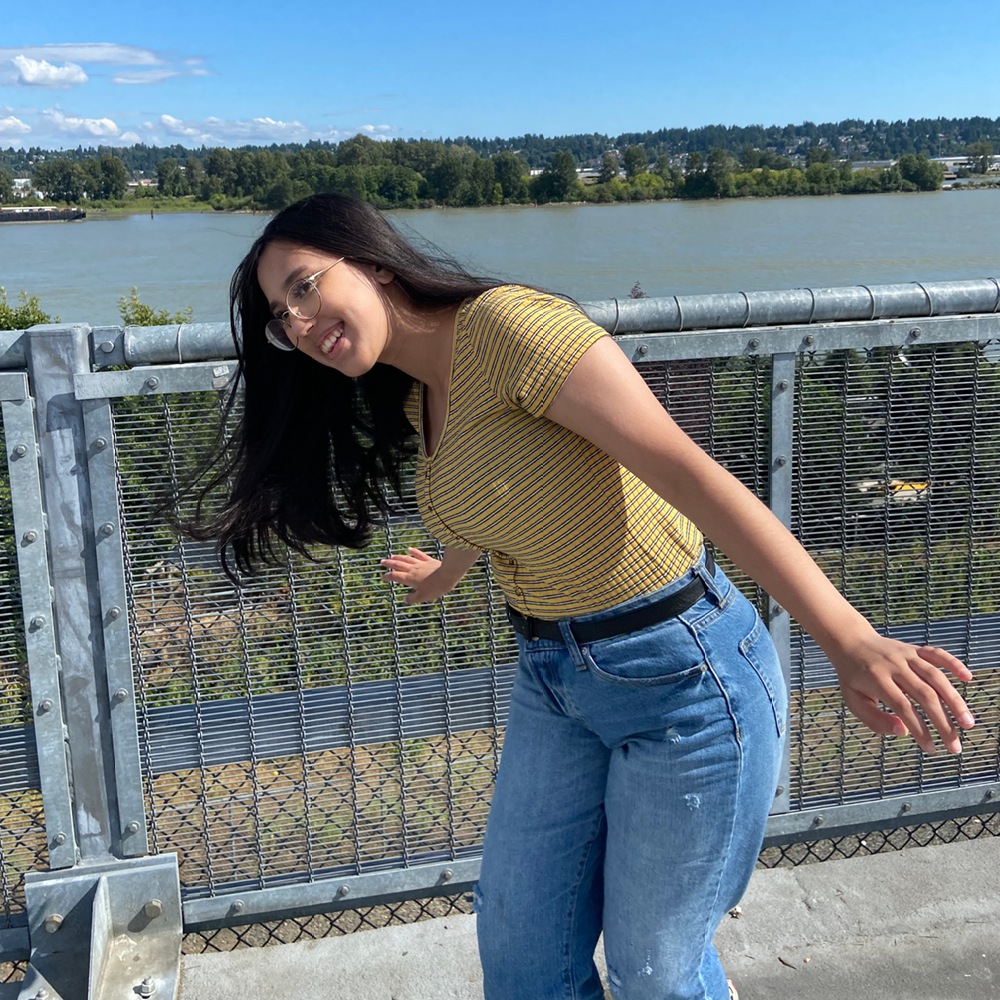 Young woman wearing yellow shirt and jeans caught candidly in motion with water and trees in the background.