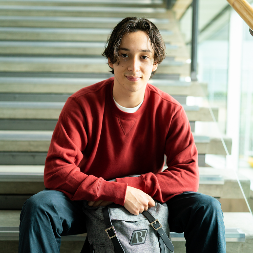 Young man in a red sweater and dark blue jeans sits on the steps of a staircase.