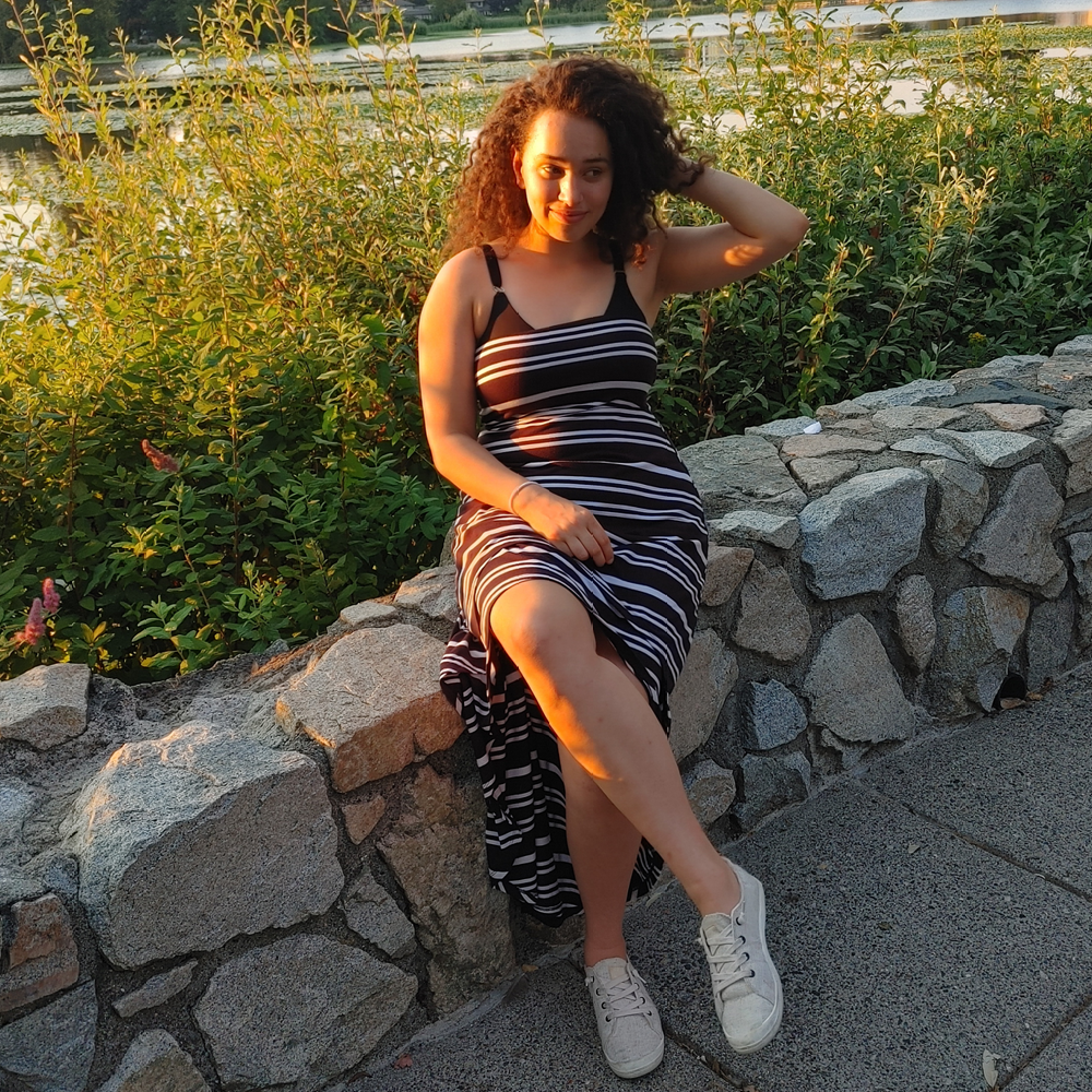 Young woman wearing a striped dress sits on a wall made of stones.
