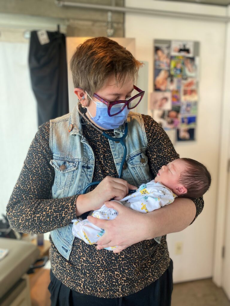 Avital, wearing a surgical mask, holds a newborn.