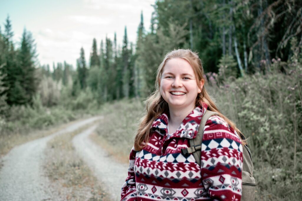 Mentor Leanne-Varney smiles wearing a colourful and patterned fleece in the forest and backcountry.