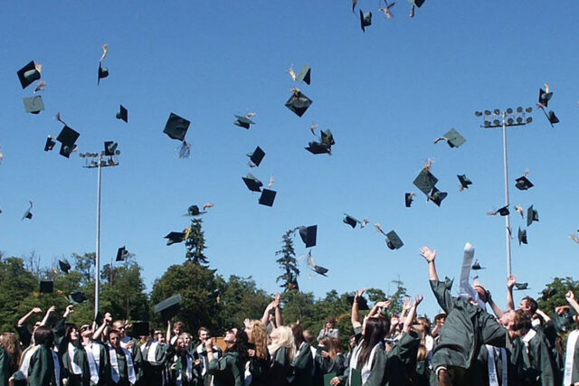 A large group of graduates throw their graduation caps in the air on a sunny day.