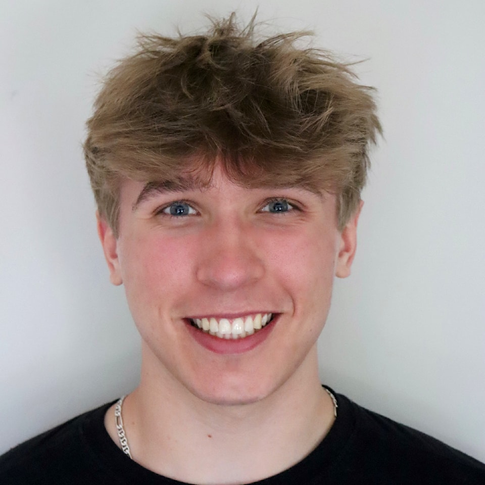 Young man with blonde hair poses in front of white wall, smiling with his teeth.